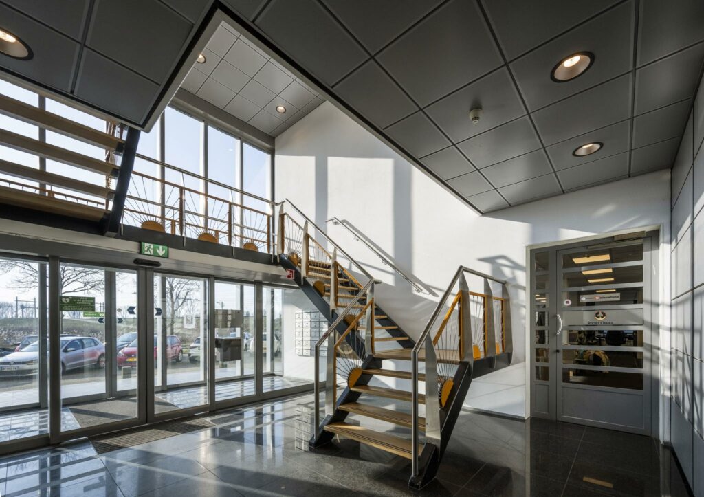 Moderne entreehal aan de Joan Muyskenweg met glazen schuifdeuren, een stalen trap en veel natuurlijk licht.